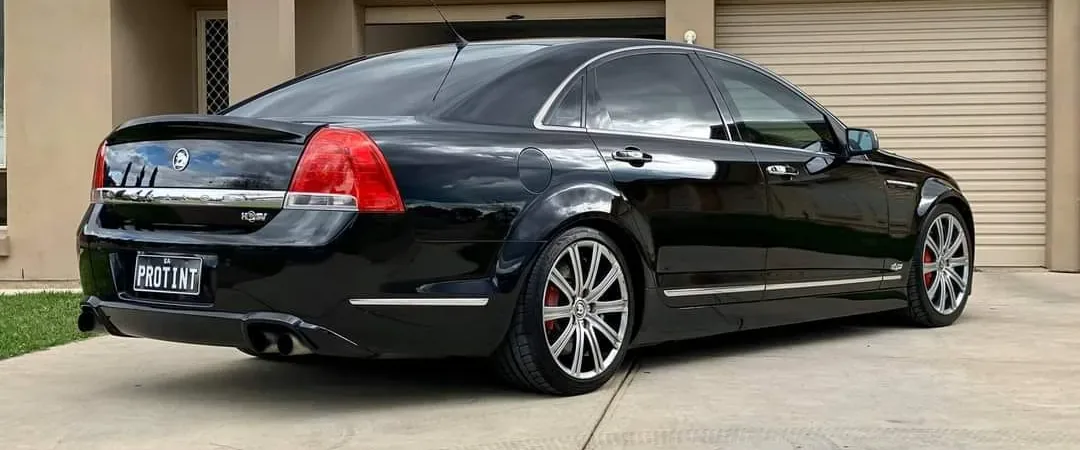 Black Holden Caprice with a PROTINT plate and dark window tint in a driveway